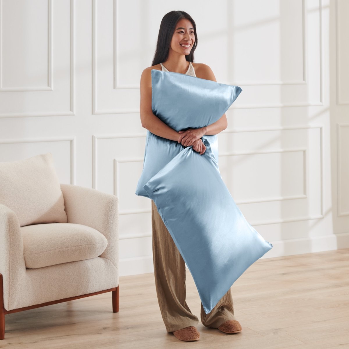Woman holding 2 pillows with satin pillowcases on them