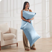 A woman has 2 pillows in her hands and they have satin pillowcases on them