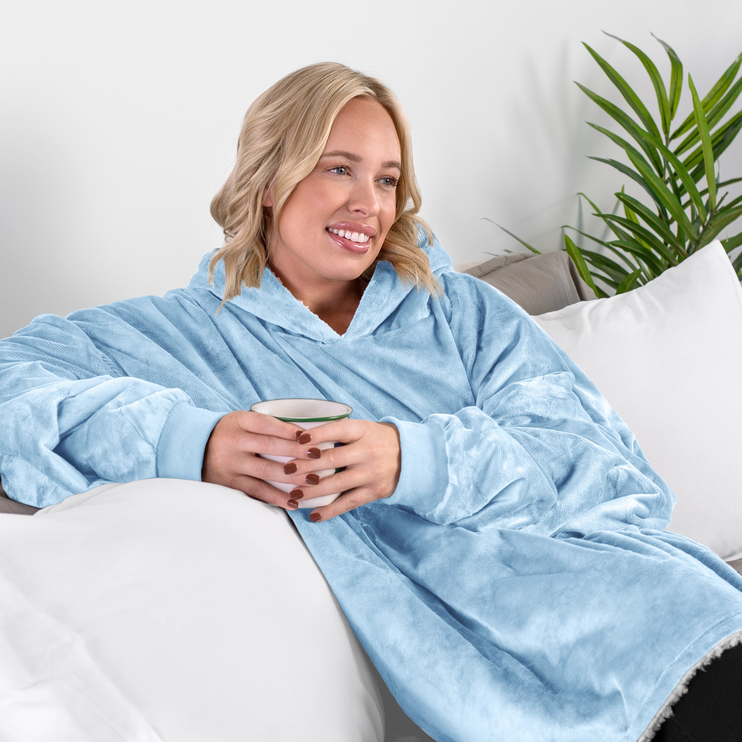 A woman sitting on a couch holding a mug wearing a sherpa blanket.