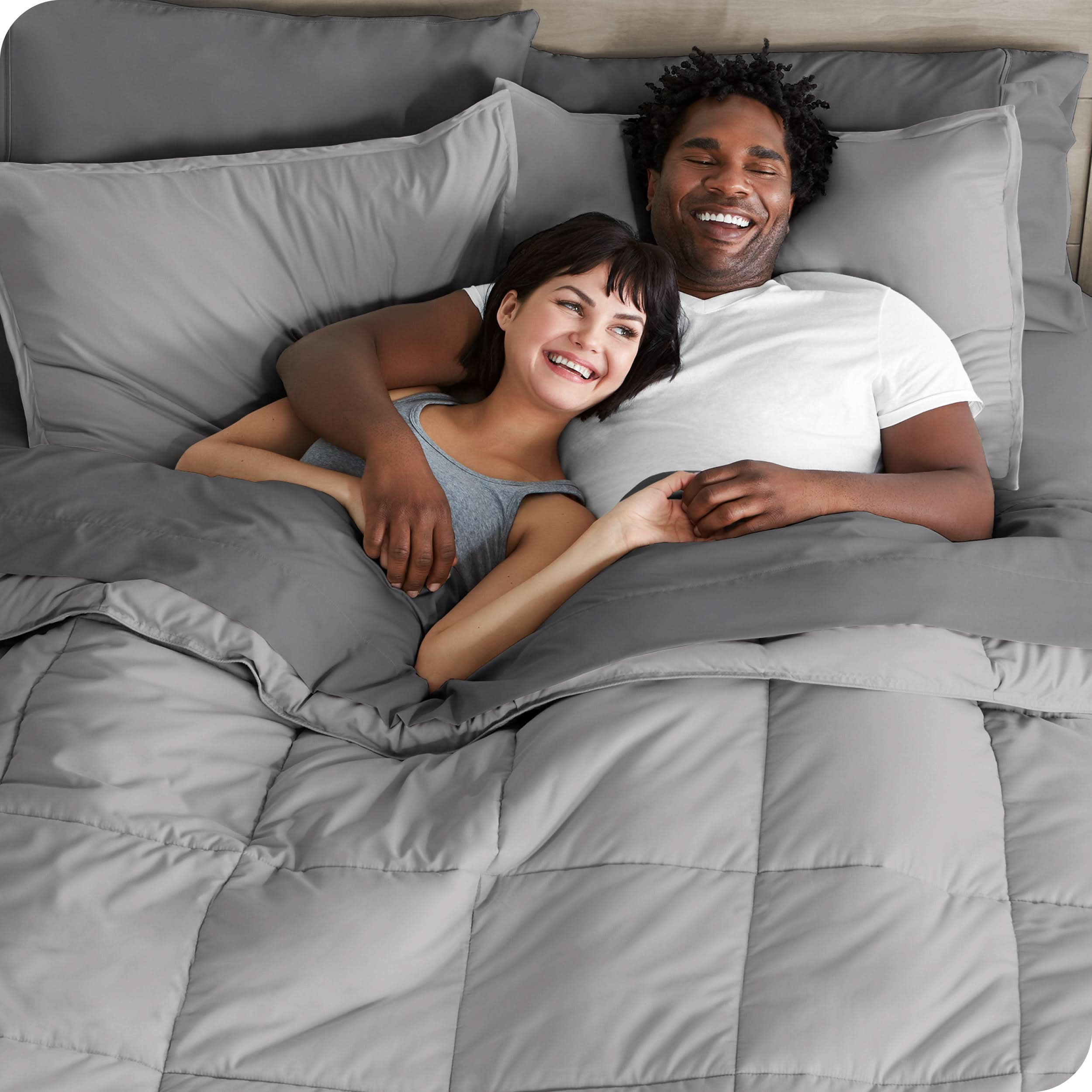 A couple is lying in bed with a comforter and sheets over them