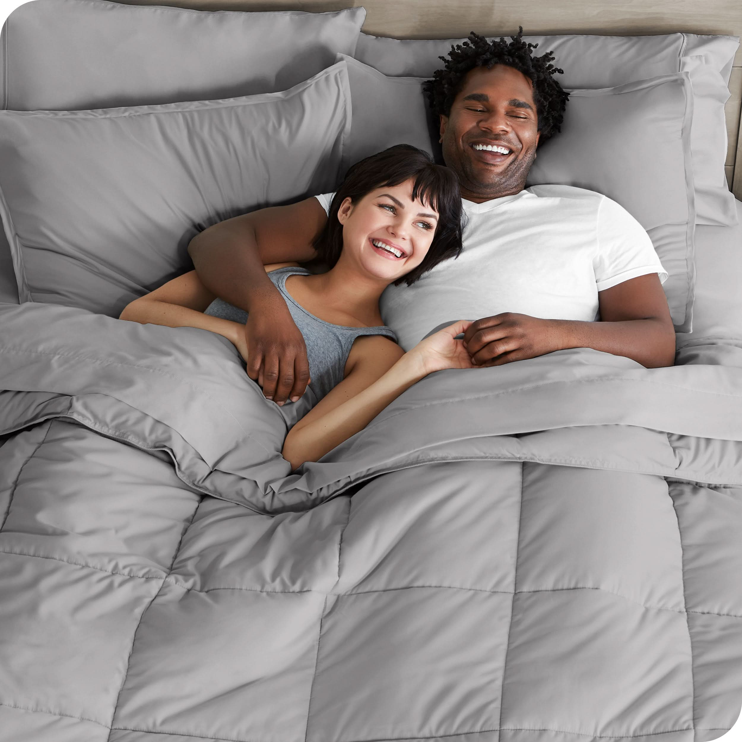 A couple is lying in bed with a comforter and sheets over them