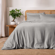 Light grey bedding on a bed with a wicker headboard in a bedroom setting.
