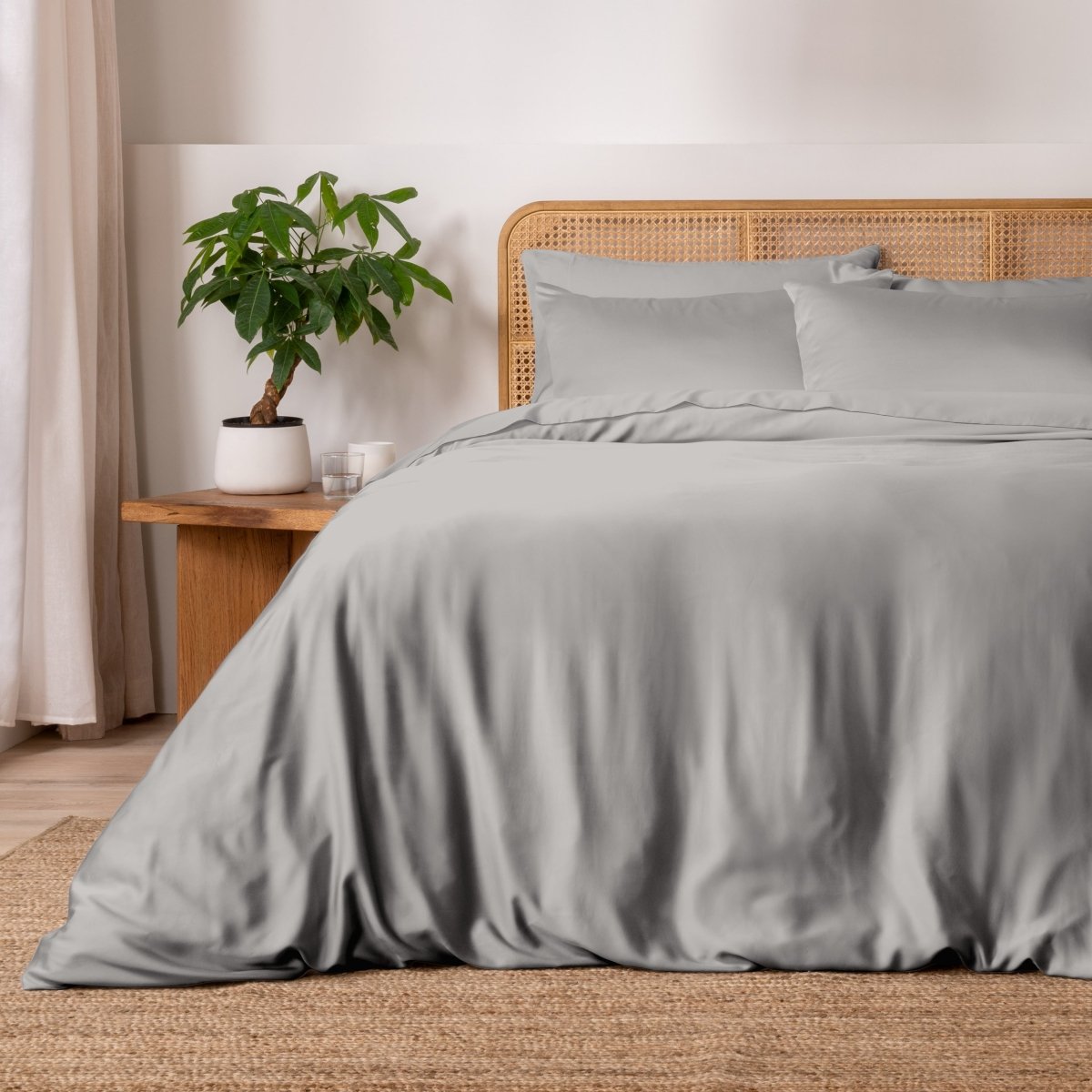 Light grey bedding on a bed with a wicker headboard in a bedroom setting.
