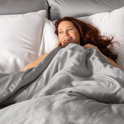 Woman lying in bed under light grey duvet cover with pillows