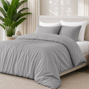 Light grey bedding set on a bed with a plant in the background