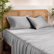 Bamboo bed sheets and pillows on a bed with a wicker headboard in a room with plants.