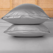 Two grey pillows stacked on a bed with a woven headboard.
