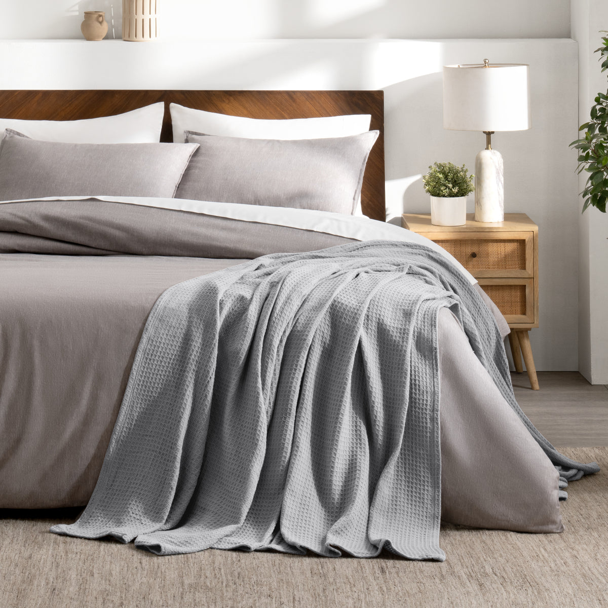 Bed with gray bedding and a throw blanket in a bedroom setting.