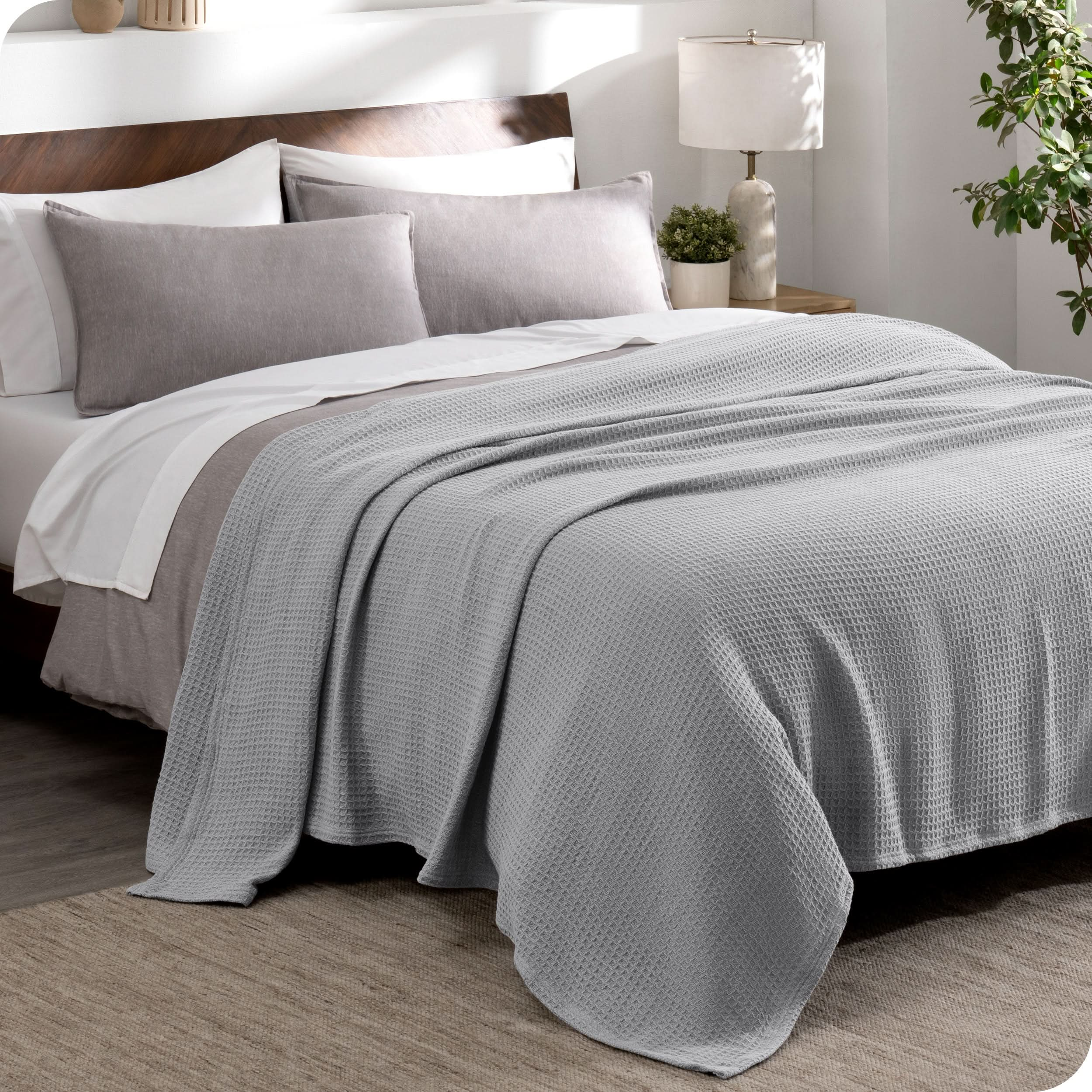 A cotton waffle blanket draped over the top of a bed made with a duvet set