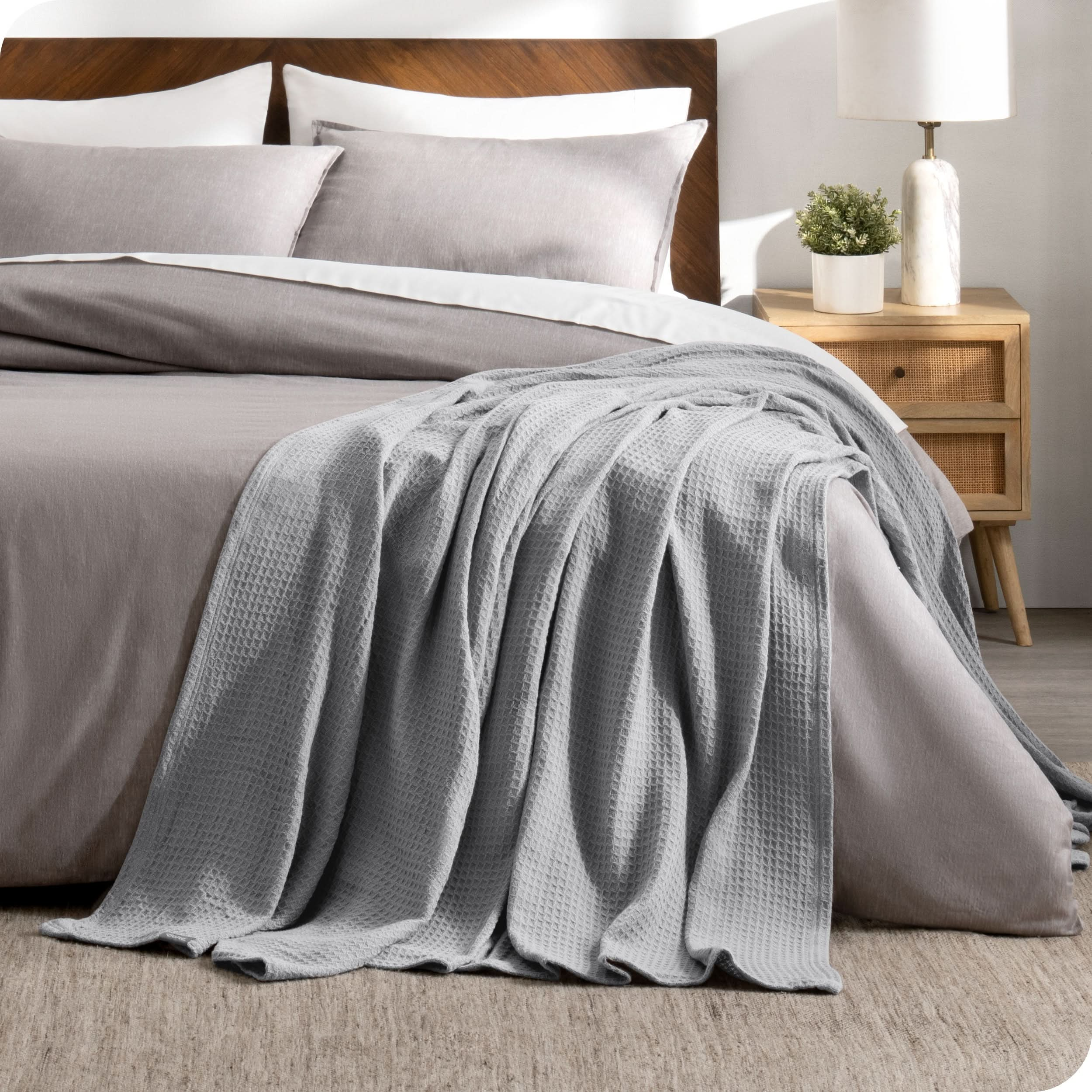 A cotton waffle blanket is on the corner of a bed. It is hanging down the side and end of the bed.