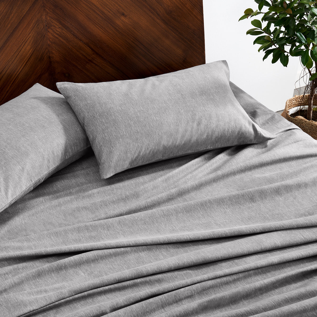 Gray bedding set on a bed with a wooden headboard and plant in the background