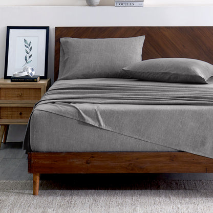 Gray bedding set on a bed with a wooden headboard and plant in the background
