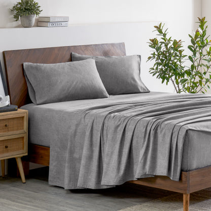 Gray bedding set on a bed with a wooden headboard and plant in the background