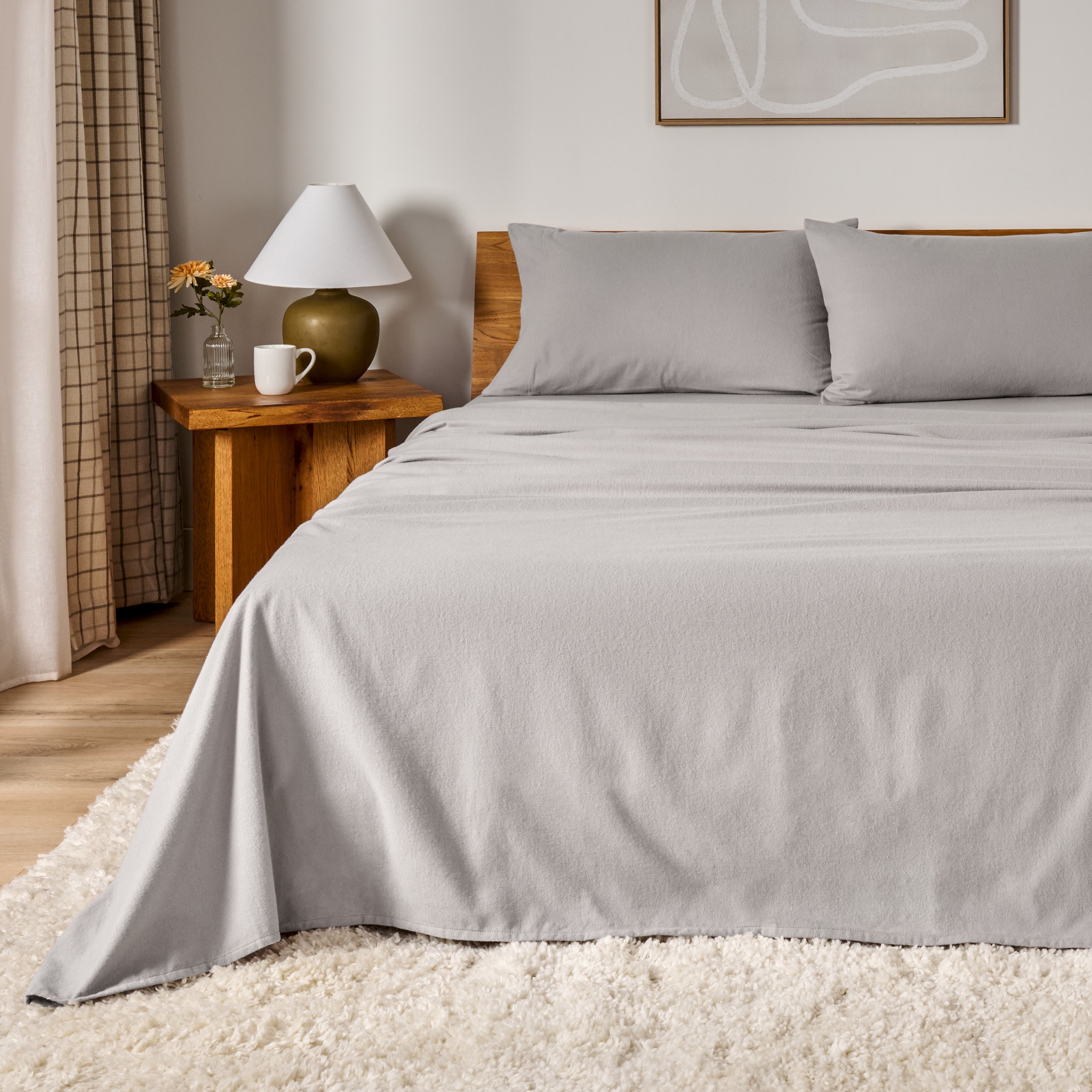 A bed dressed in flannel sheet set in a bedroom with a wooden headboard, bedside table and lamp