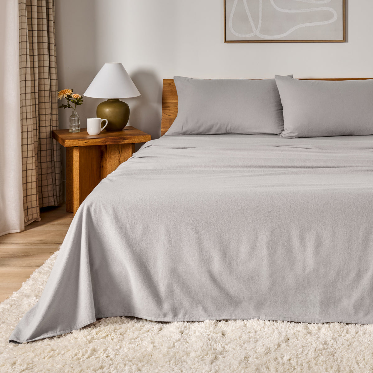 A bed dressed in flannel sheet set in a bedroom with a wooden headboard, bedside table and lamp