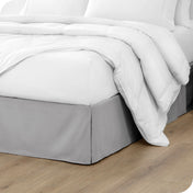 A modern bed with a microfiber bed skirt with pleats on the corners and midway on each side.