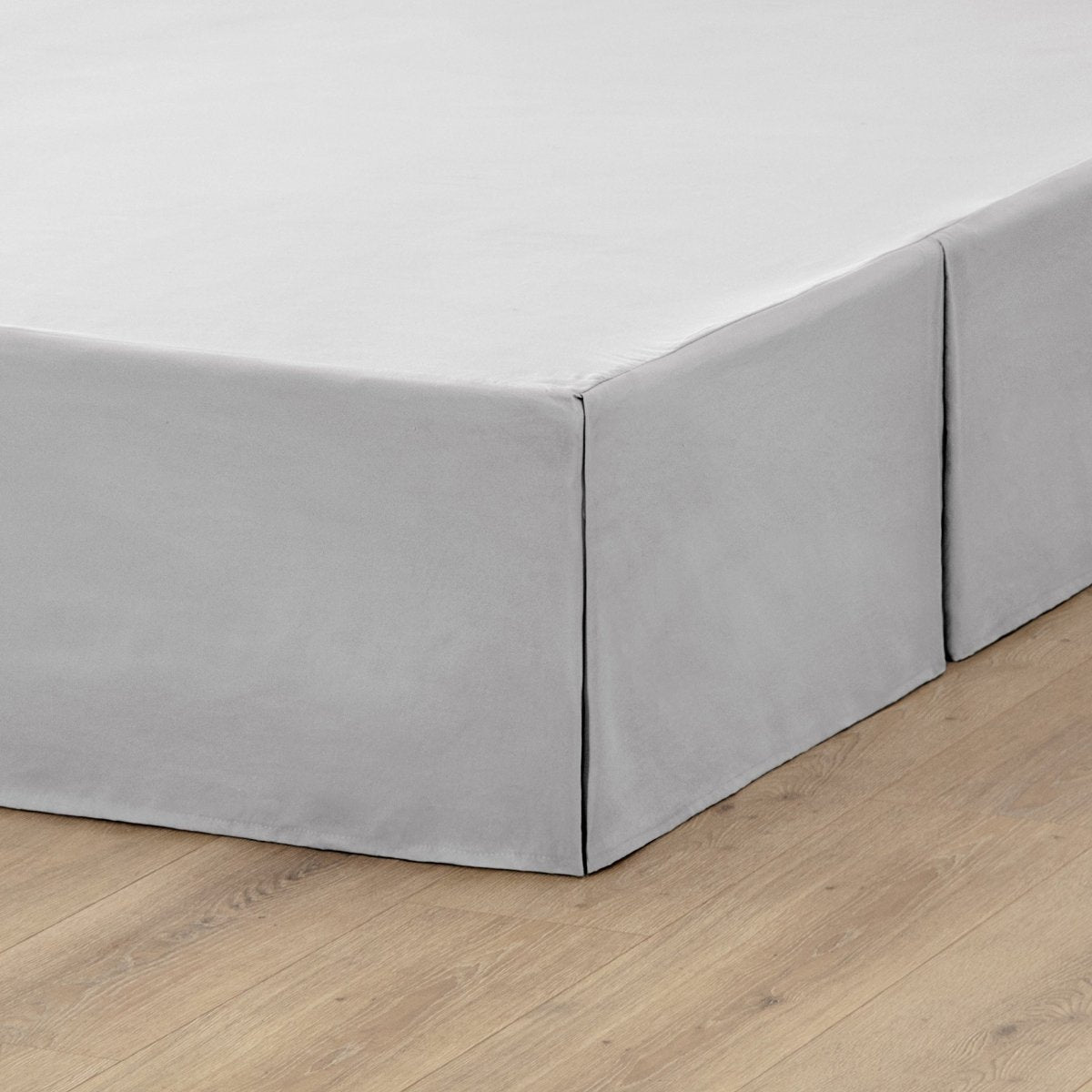 The corner of a box spring with a pleated bed skirt on it