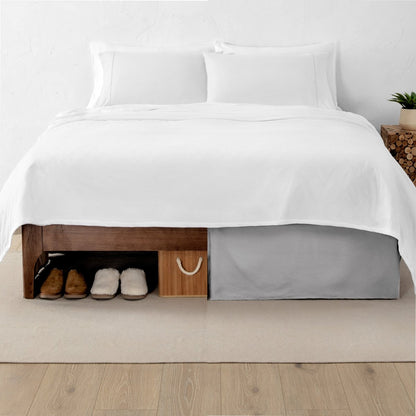 One side of a bed has shoes and a box under it while the other side has a bed skirt so that under the bed is hidden from view