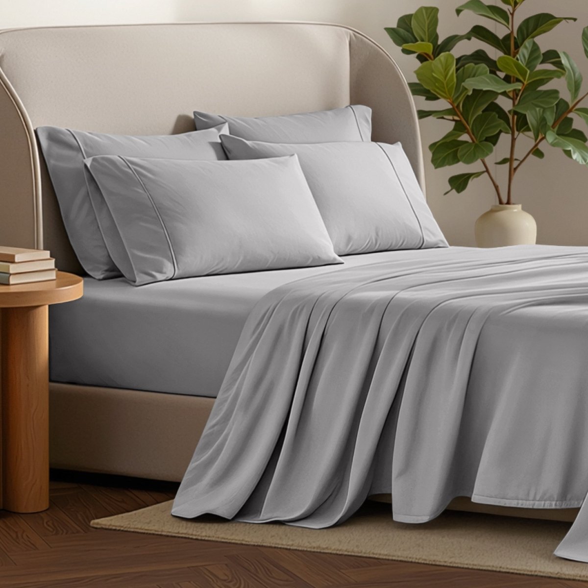 Bed sheets and pillows on a bed with a plant and side table in the background.
