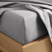 A close-up of a fitted sheet covering the corner of a bed frame, with matching top sheet draped over it.