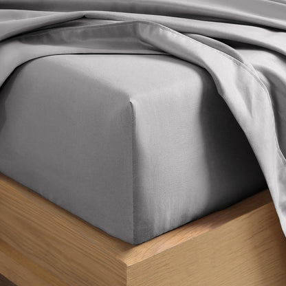 A close-up of a fitted sheet covering the corner of a bed frame, with matching top sheet draped over it.