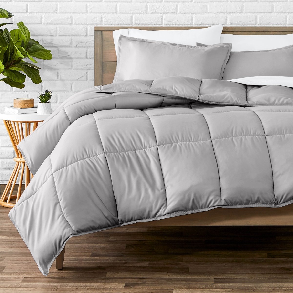 Comforter set on a bed with a white brick wall and plant in the background