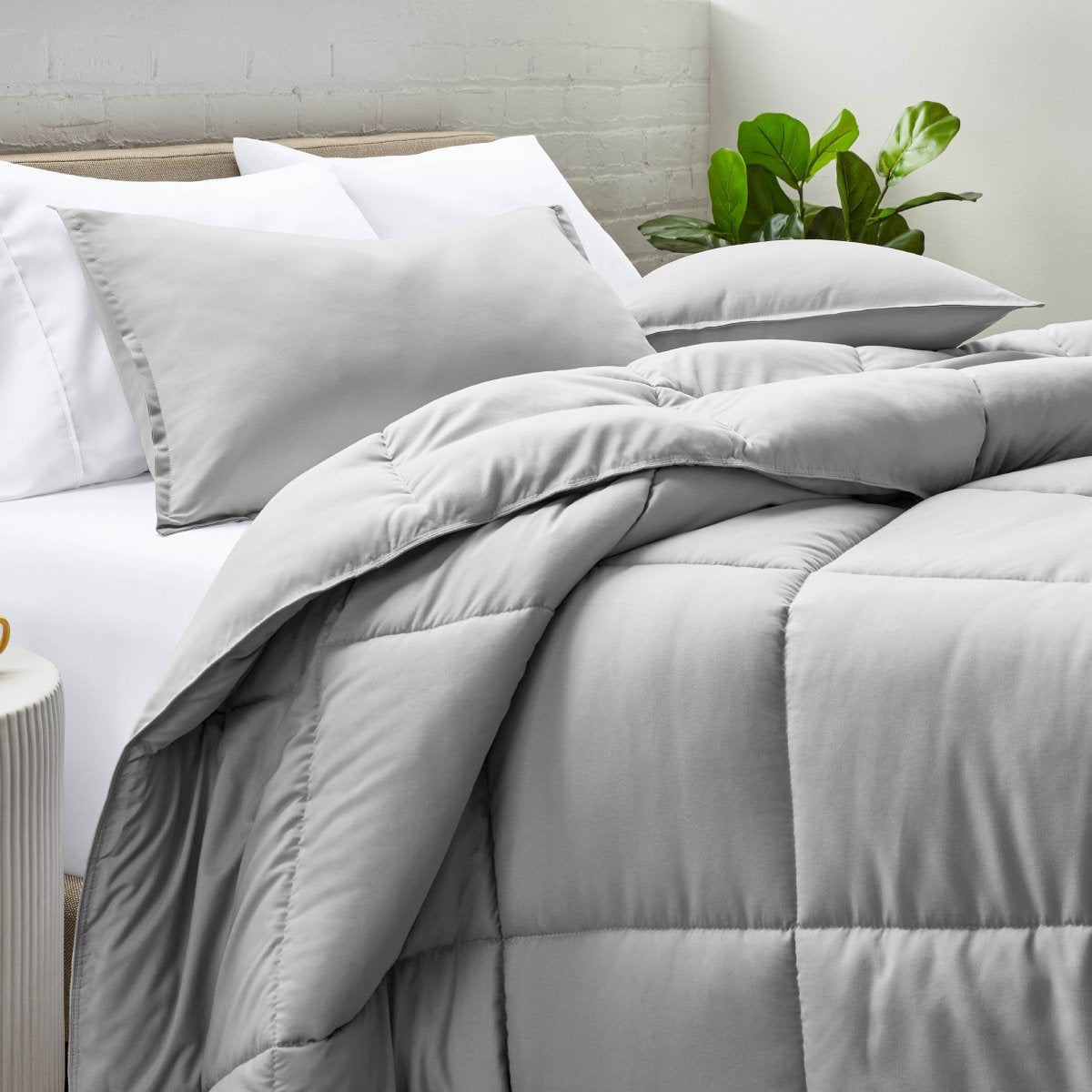 Comforter and pillow shams on a bed with a white brick wall and plant in the background