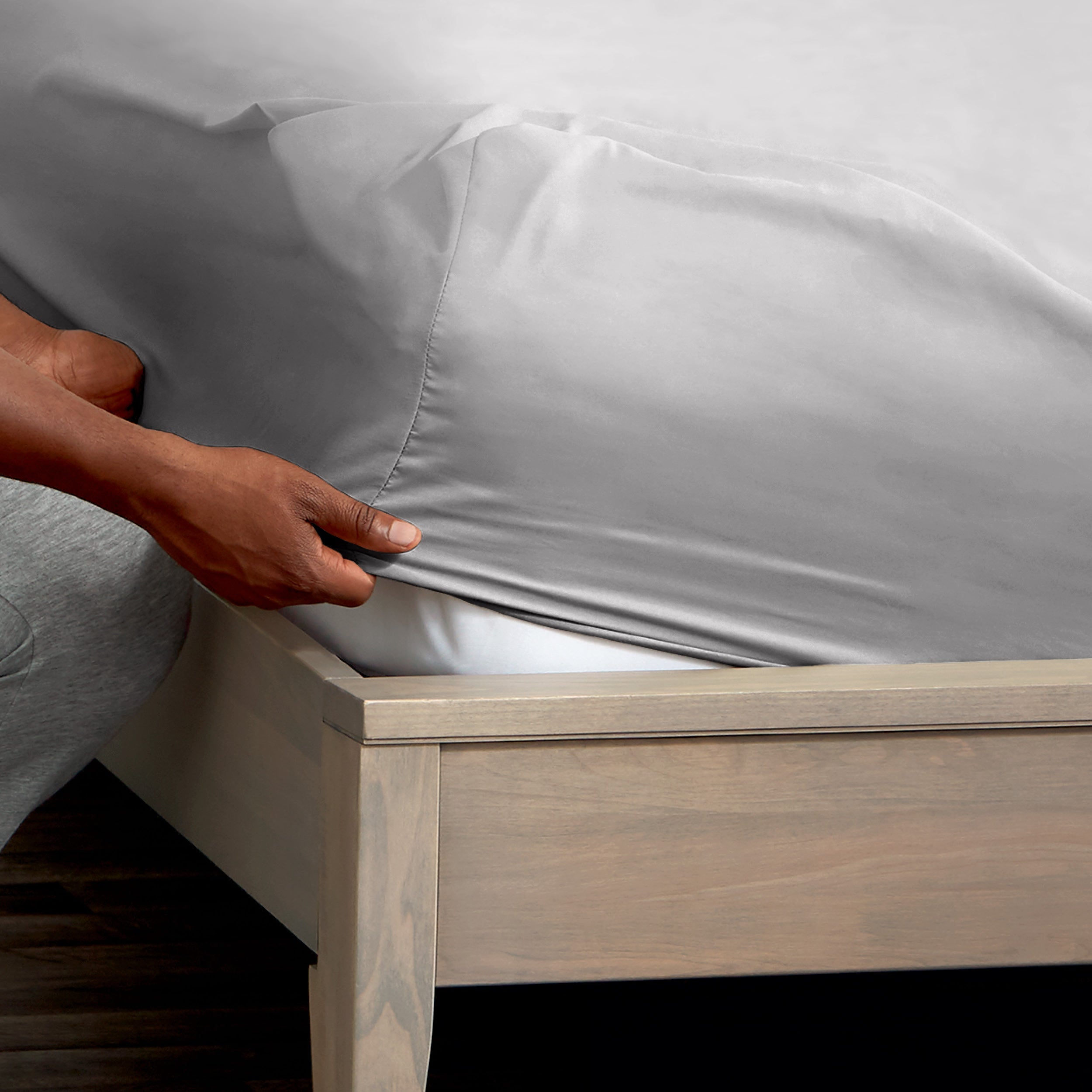 A man is putting a fitted sheet on a bed