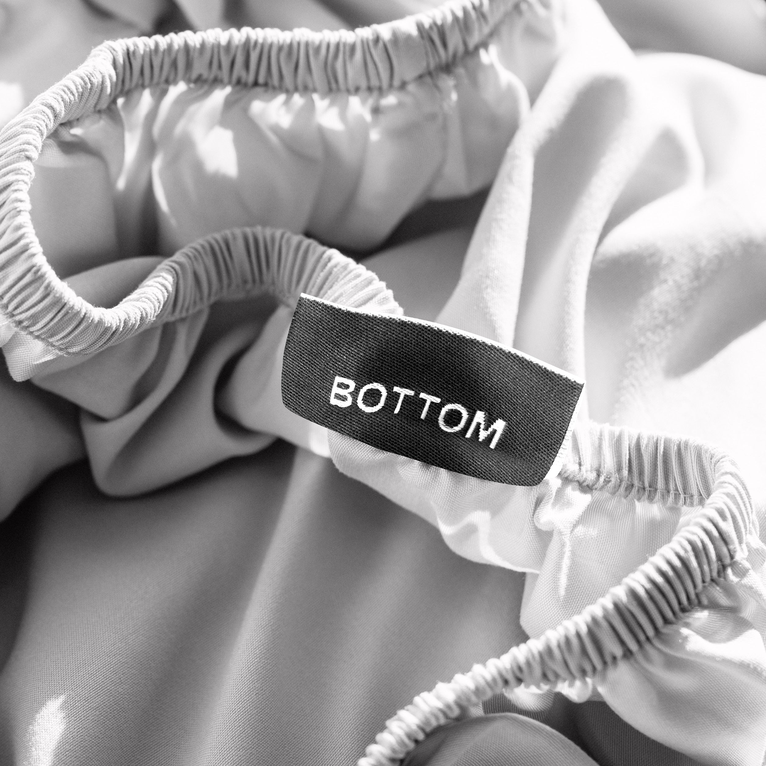 A close-up of a fitted sheet with a label printed with the word 'BOTTOM' in white.