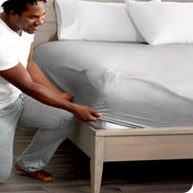 A man is kneeling while putting a fitted sheet on a bed