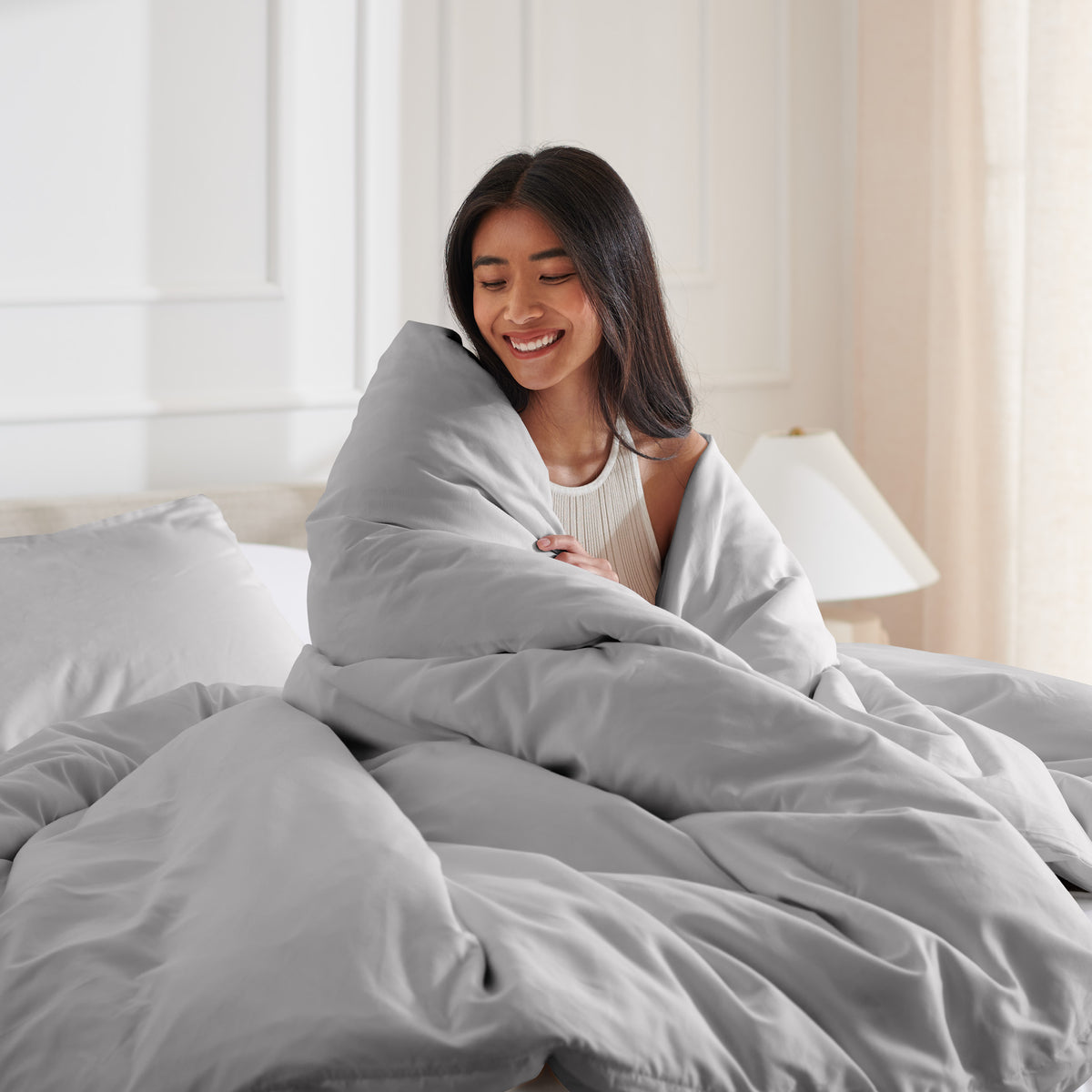 Woman smiling under duvet cover set in a bedroom setting