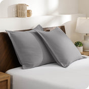 Two pillows with shams on a bed in a bedroom setting with a lamp and decor items.