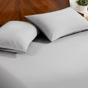 Fitted sheet and pillowcase set on a bed with a dark wood headboard and a small potted plant in the background.