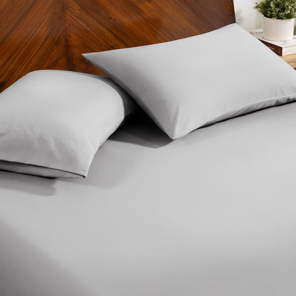 Fitted sheet and pillowcase set on a bed with a dark wood headboard and a small potted plant in the background.