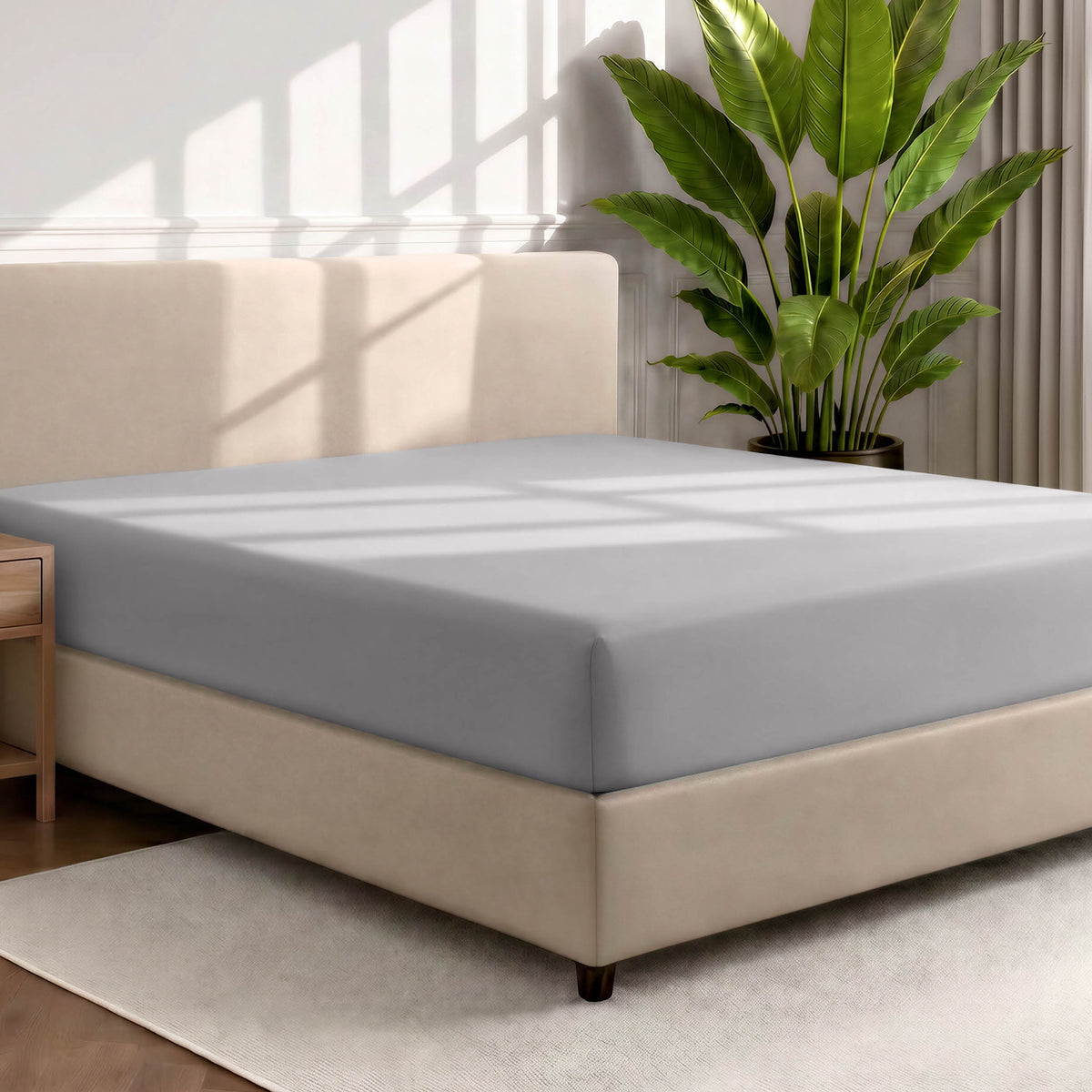 Bed with a fitted sheet in a room with a large plant and rug