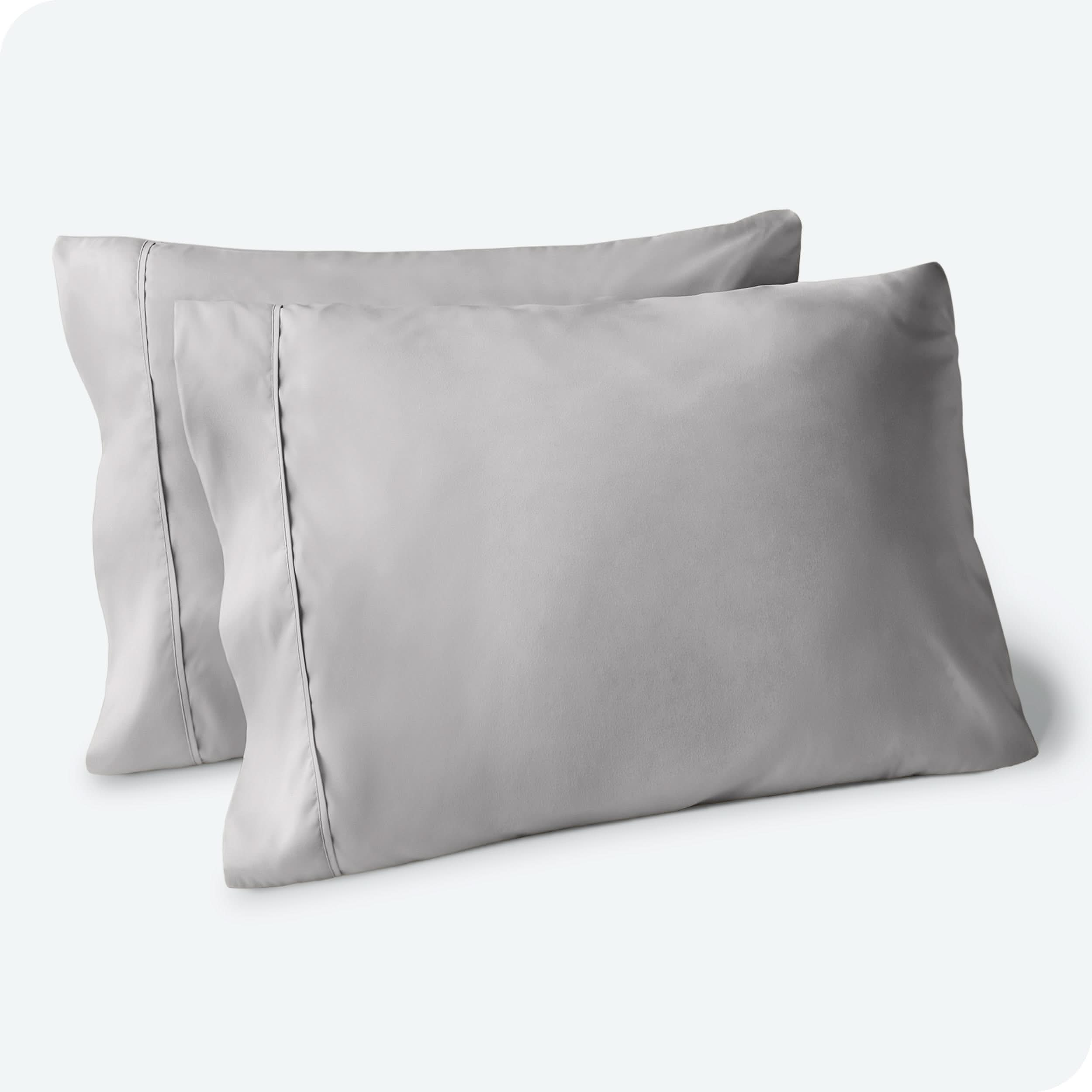 Two pillows on a white background with grey pillowcases on them