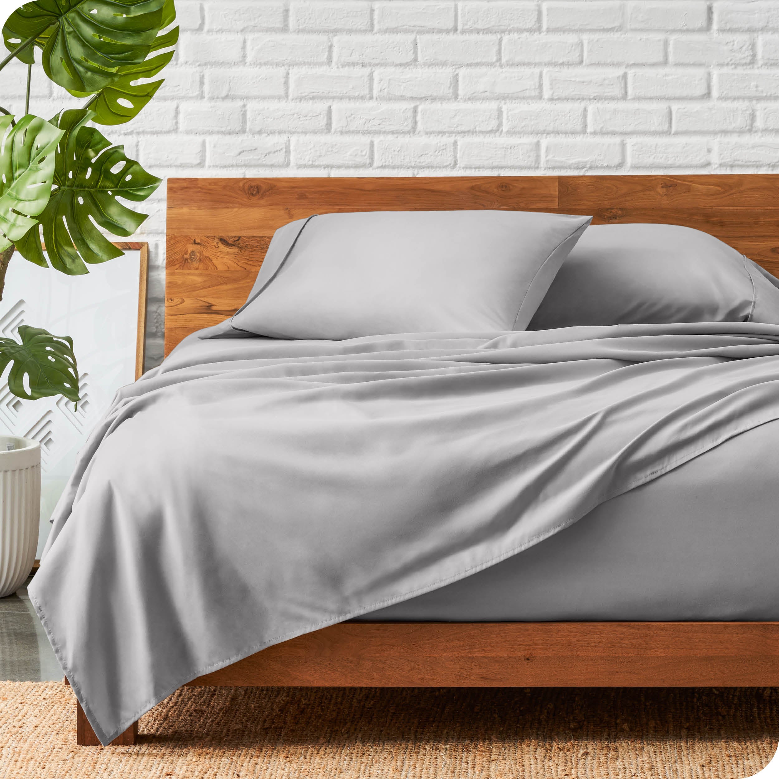 A wooden bed frame with a microfiber sheet set on the mattress.