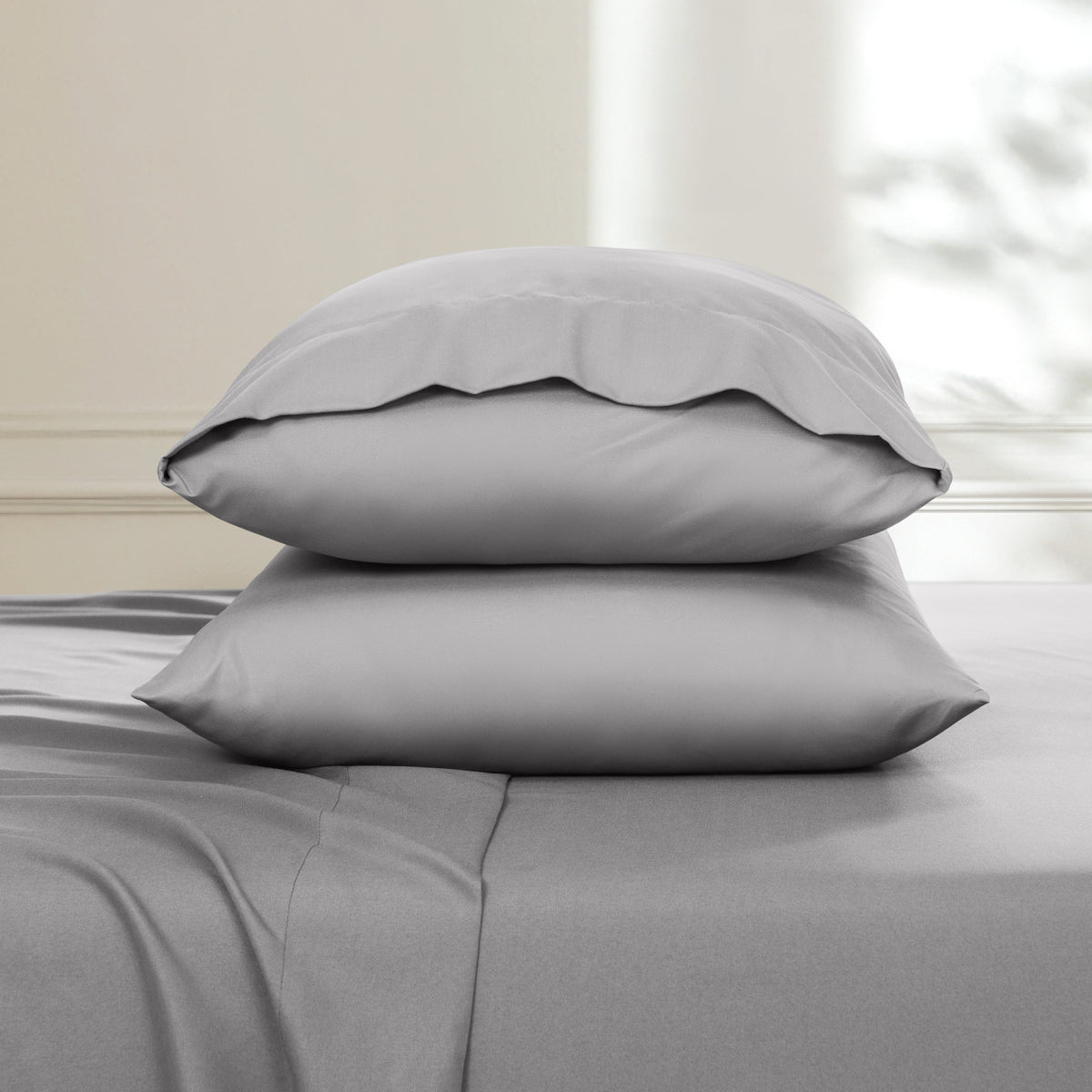 Two pillows stacked on a bed with a neutral background