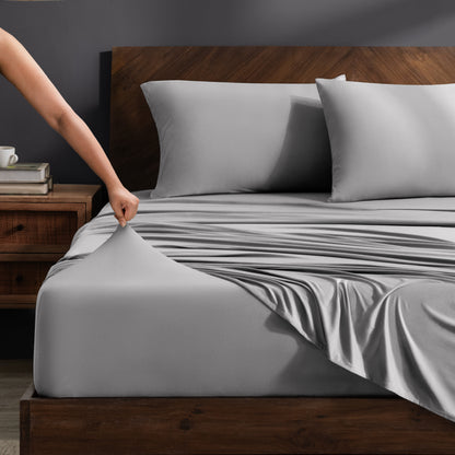 Person adjusting stretch sheets on a bed with a wooden headboard.