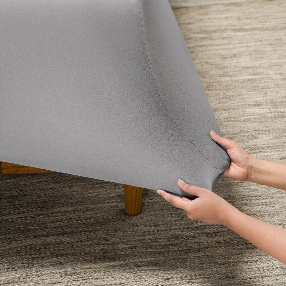 Person putting a fitted sheet on a bed on carpeted floor.