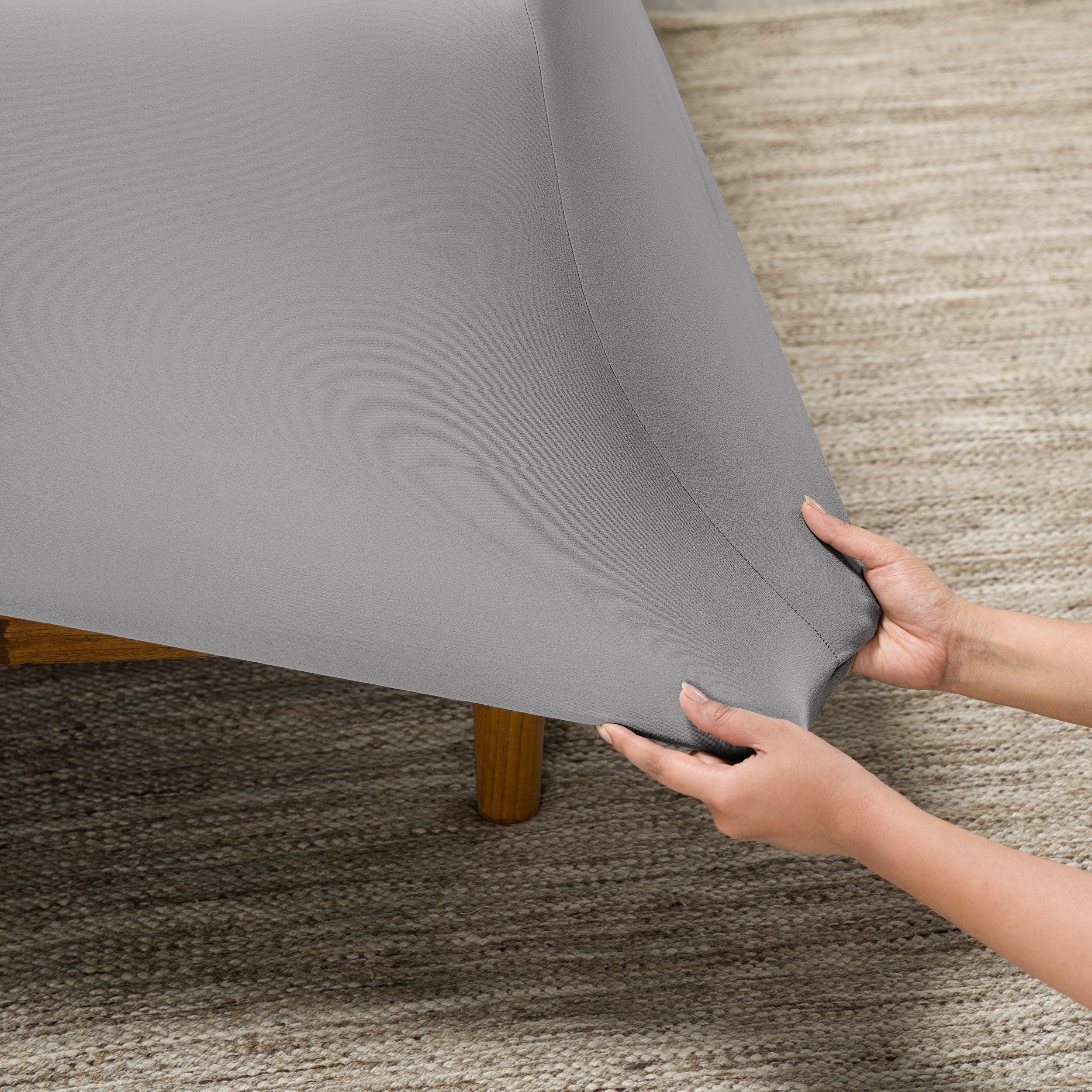 Person putting a fitted sheet on a bed on carpeted floor.