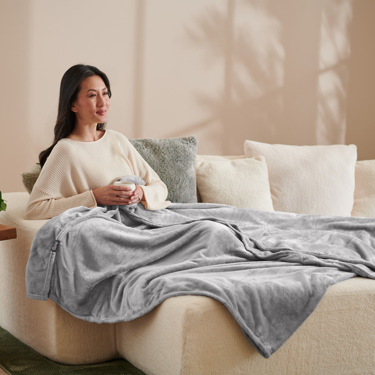 A woman sitting on a couch with a microplush blanket on her lap