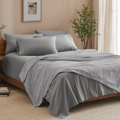 A bed made with grey sheets and a microplush blanket