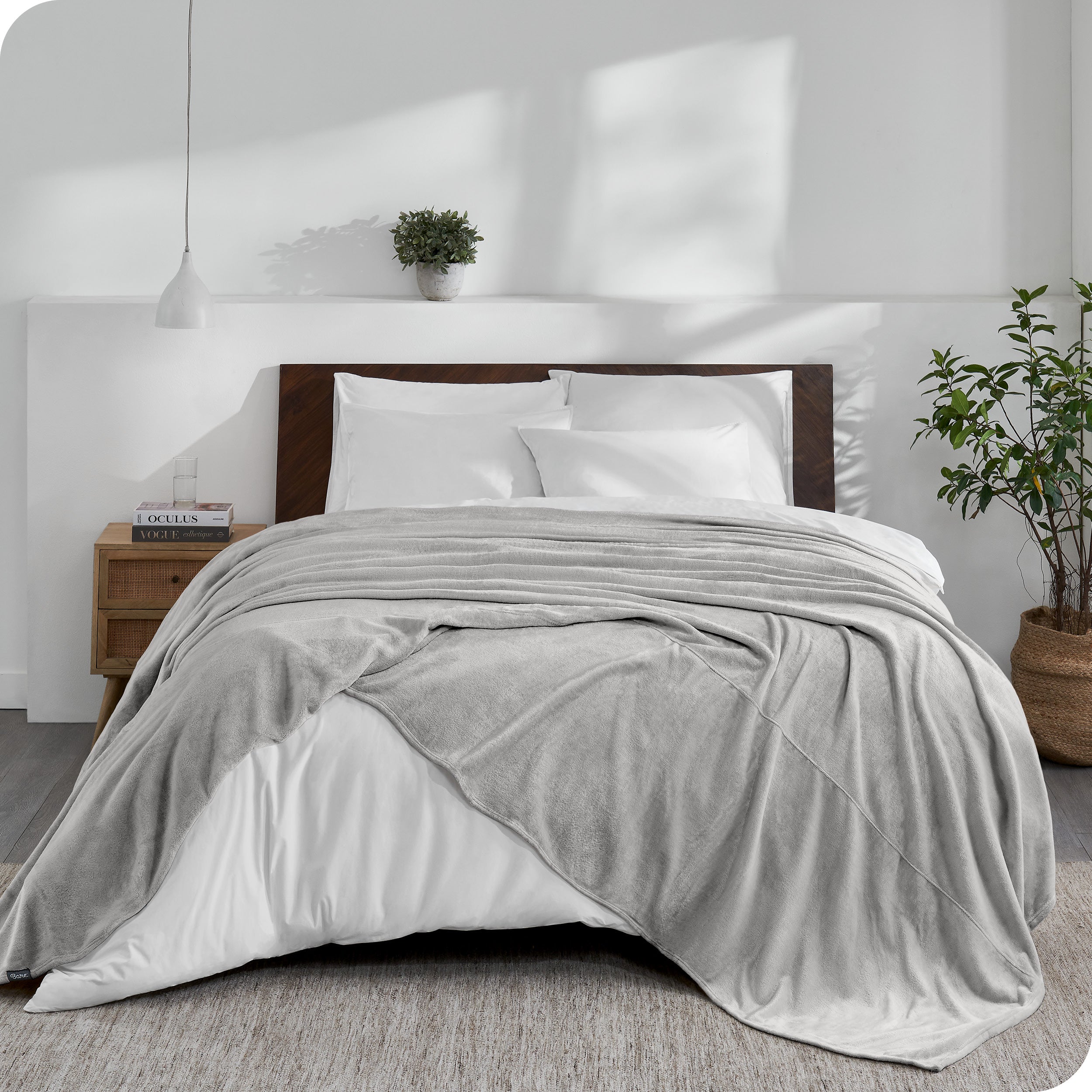 An oversized blanket on a bed made with all white bedding