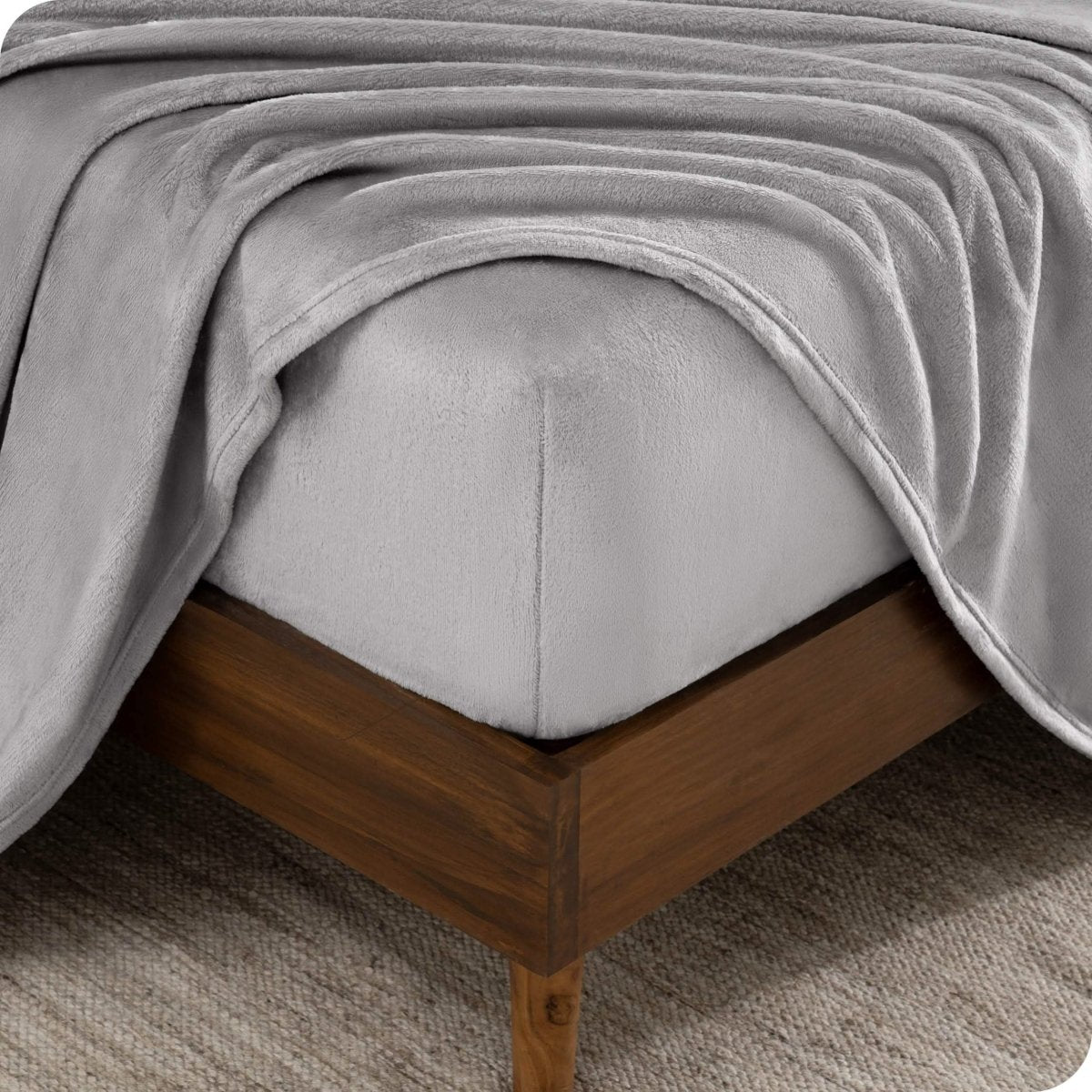 The corner of a bed frame and mattress with a fitted sheet and flat sheet on it.
