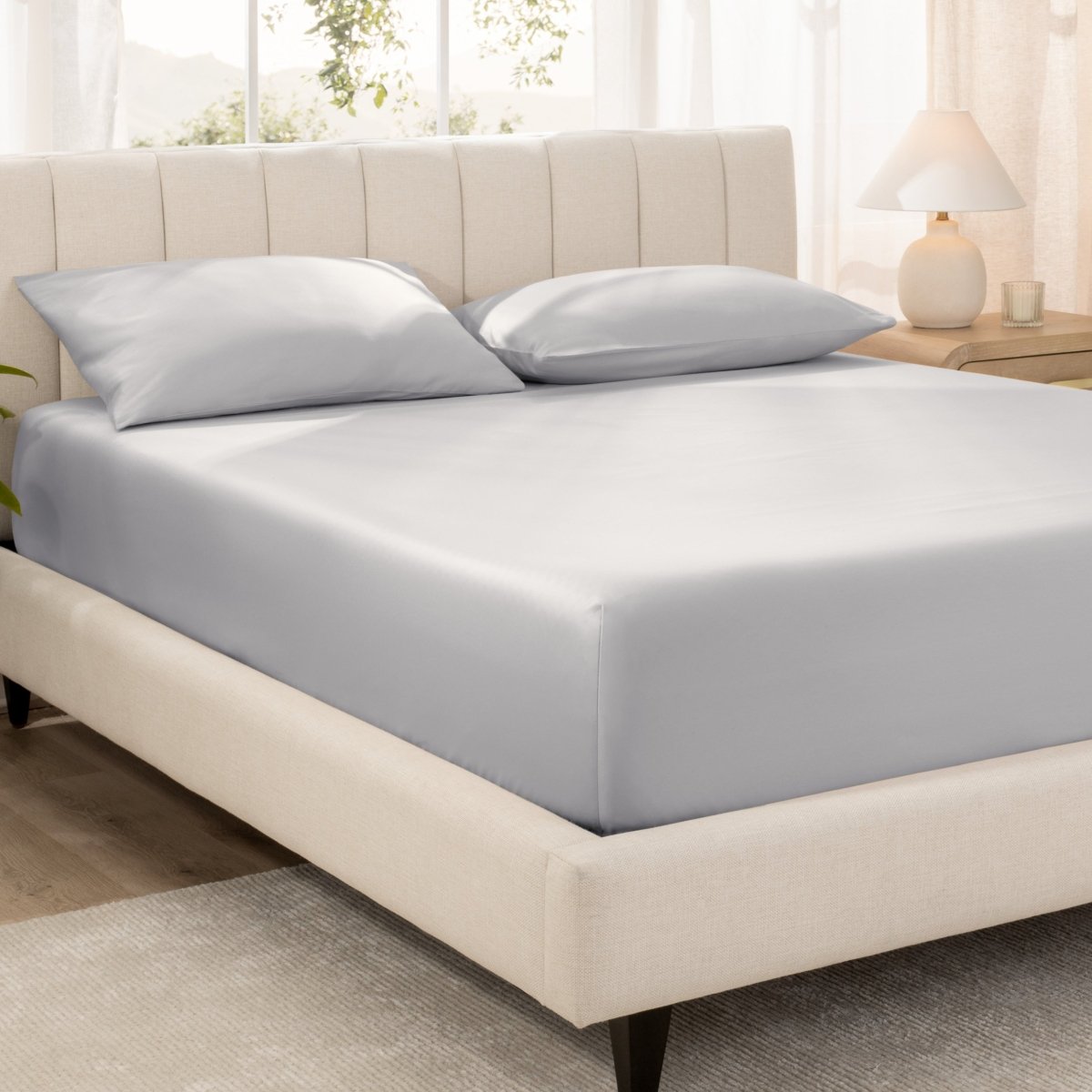 Bed with fitted sheet and pillowcases in a bright room.