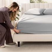 Woman adjusting a fitted sheet on a bed in a bedroom setting