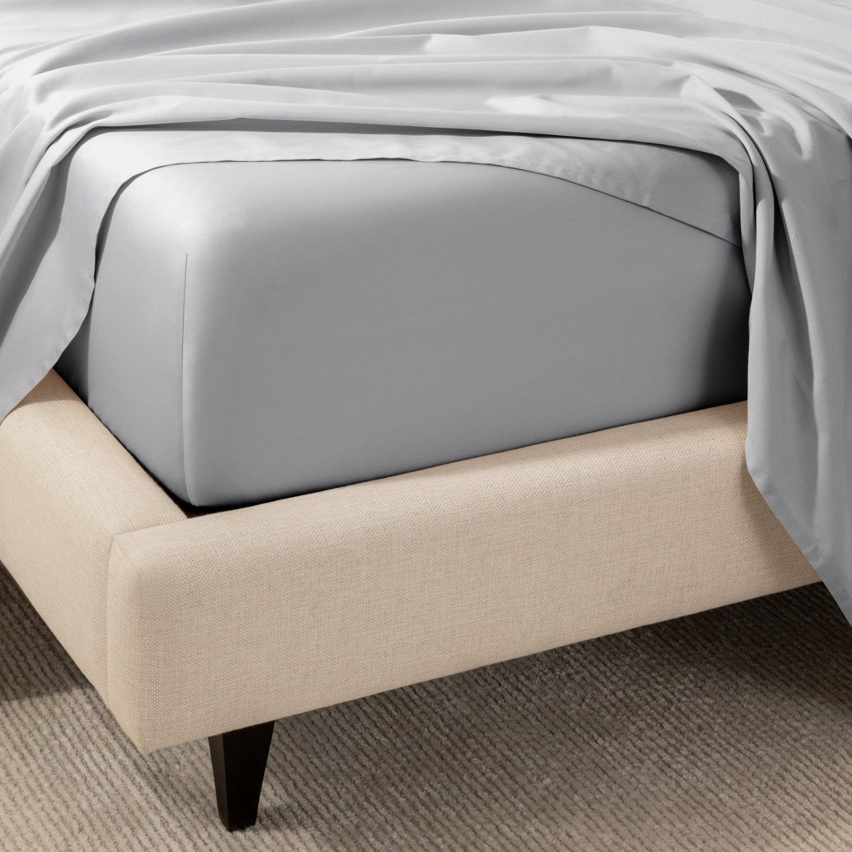 A close-up of the corner of a bed with a fitted sheet and matching flat sheet.