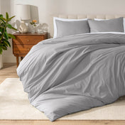 Percale bedding set on a bed in a bedroom with a wooden nightstand and lamp.