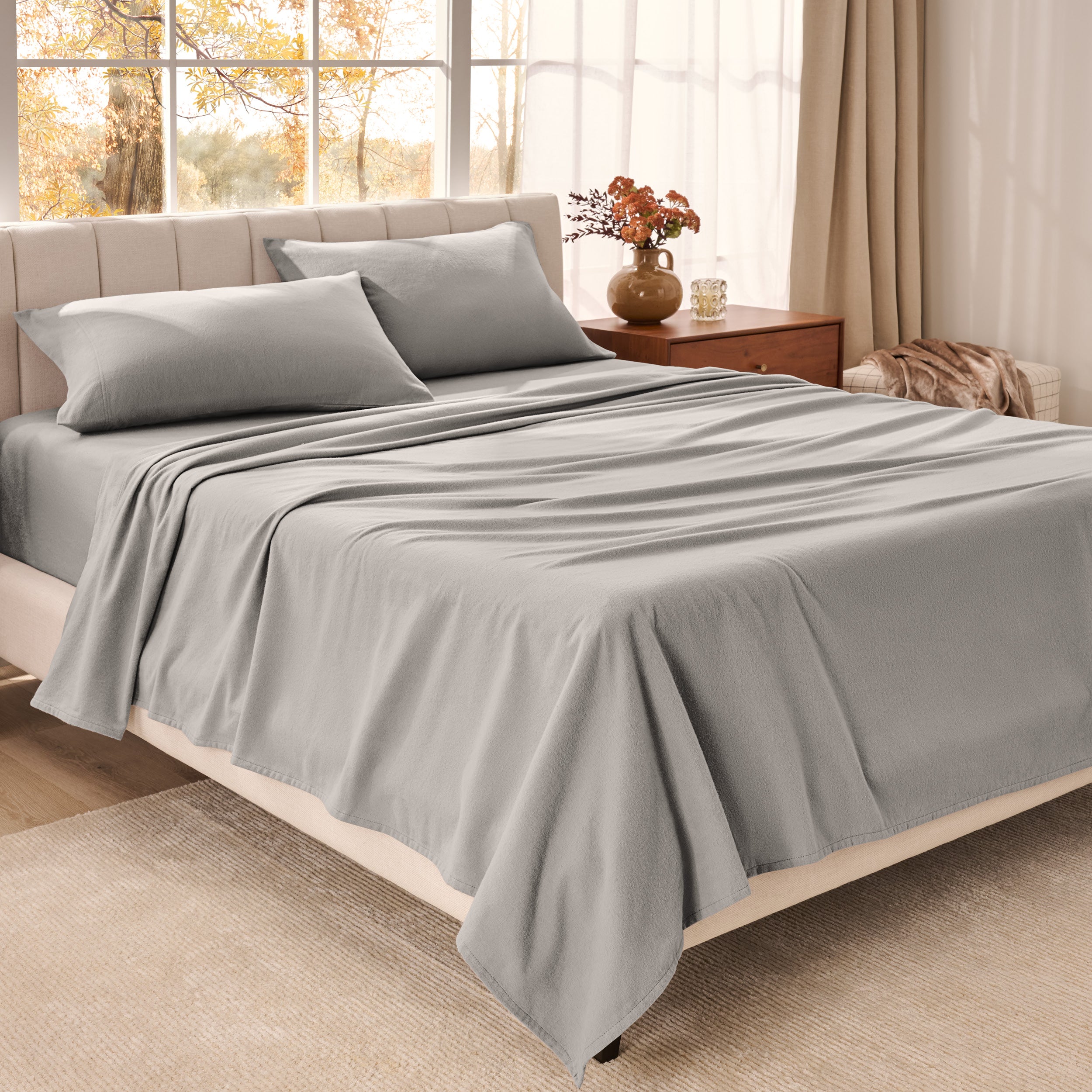 Bed sheets on a neatly made bed in a bright bedroom with large windows.